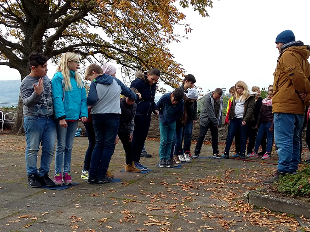 Gruppe steht im Kreis um eine Übungsmatte.